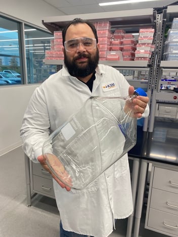 Lester in a KBI Biopharma lab coat holding up a large glass bottle he is delivering to a lab.
